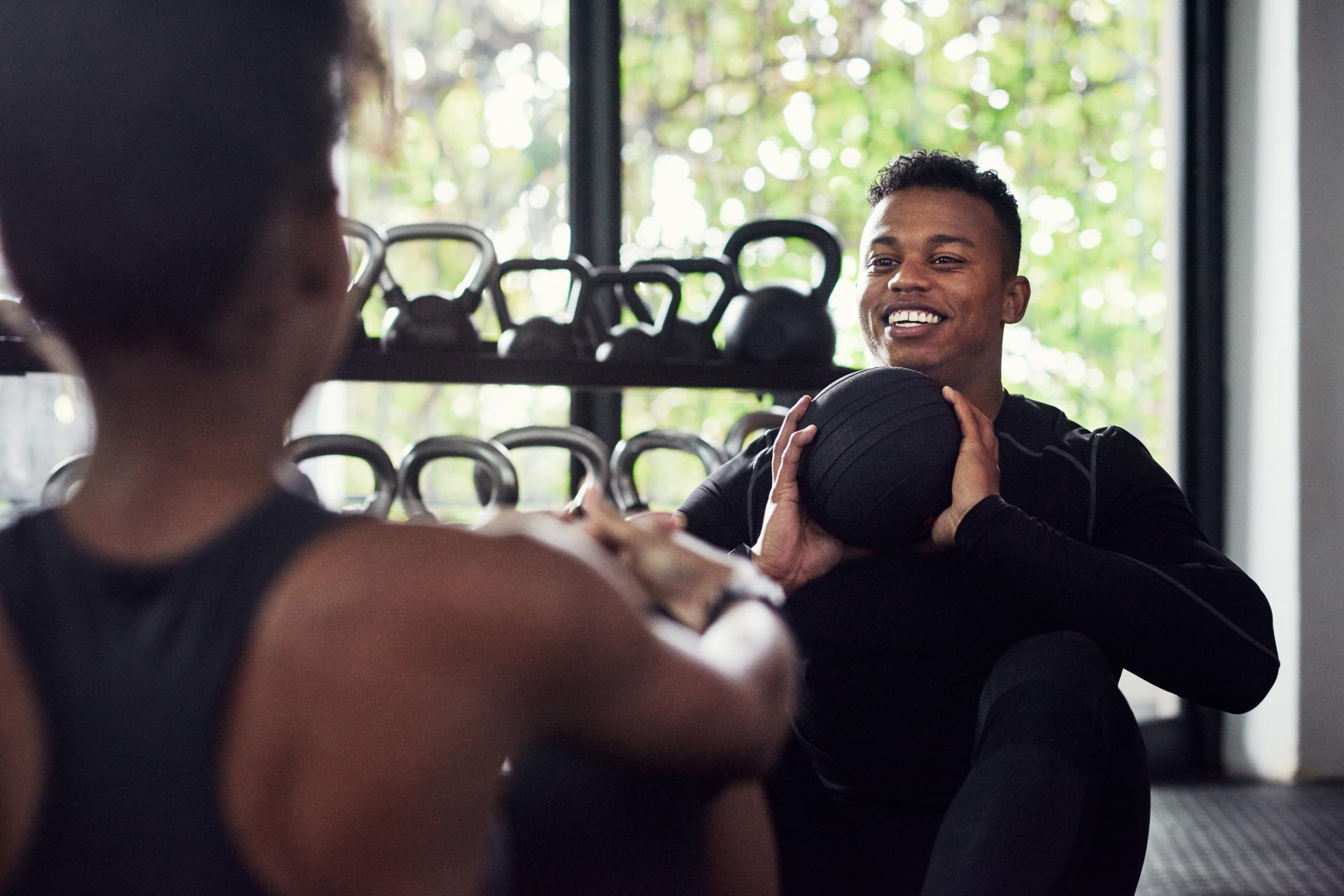 Two Black friends working out in a fitness center, one holding a kettle ball